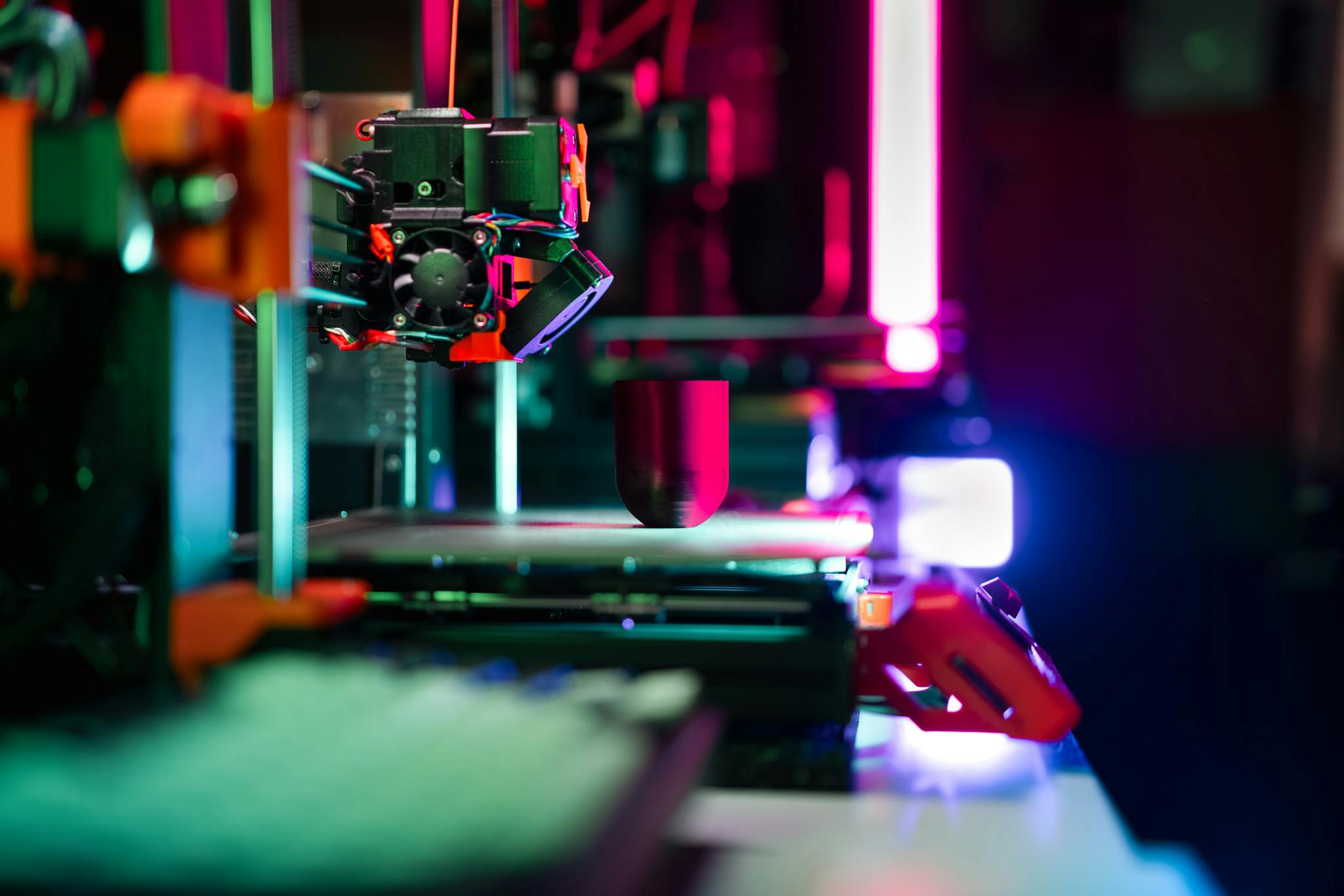 Close-up of a modern 3D printer in a workshop, highlighted by neon lighting.